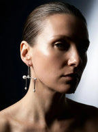 Woman wearing geometric silver and pearl statement earring against dark background